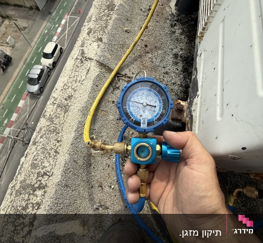 מד לחץ כחול מחובר לצינור צהוב ליד מזגן